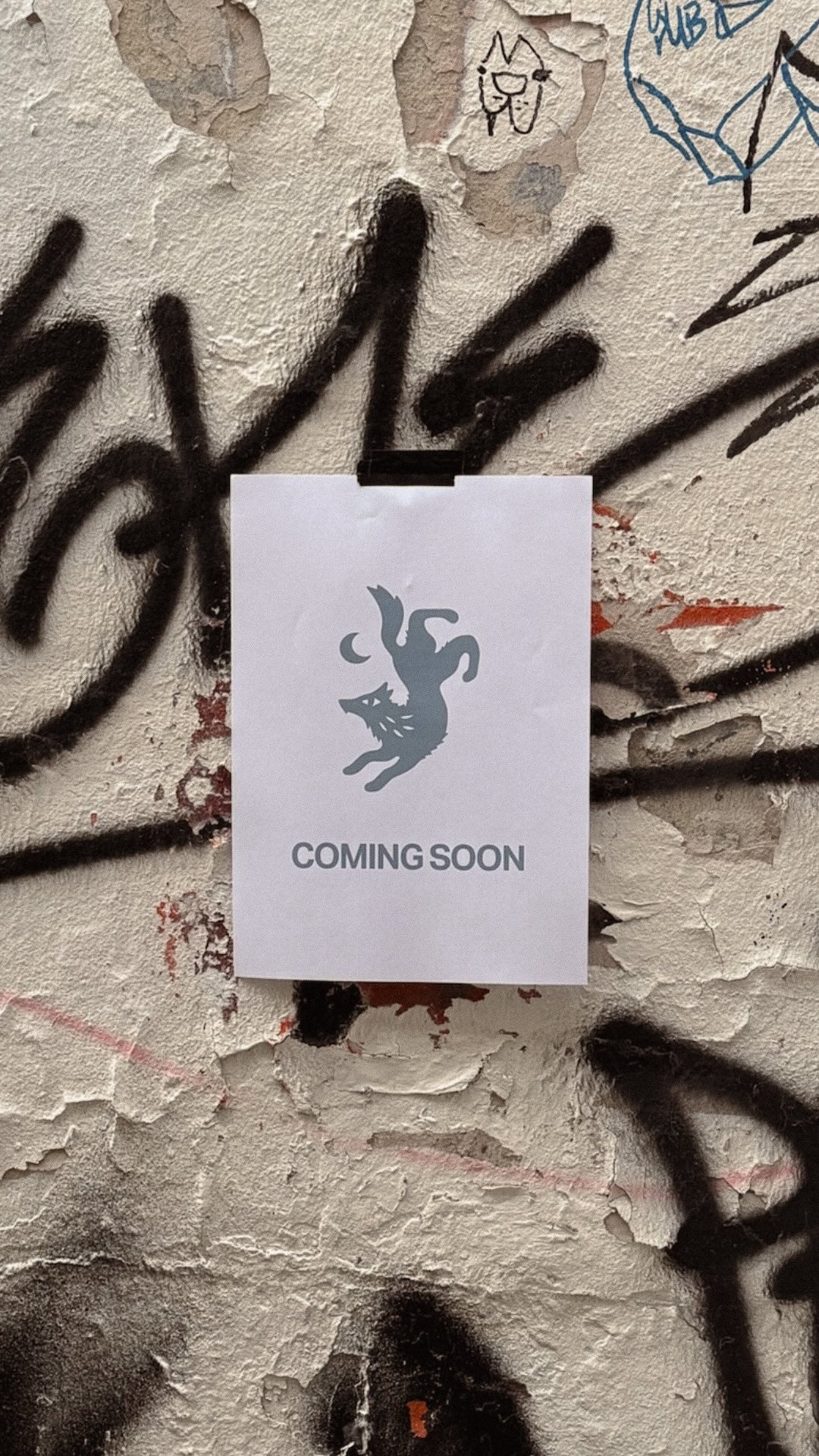 White card with 'Coming Soon' text and logo on a textured wall with graffiti.